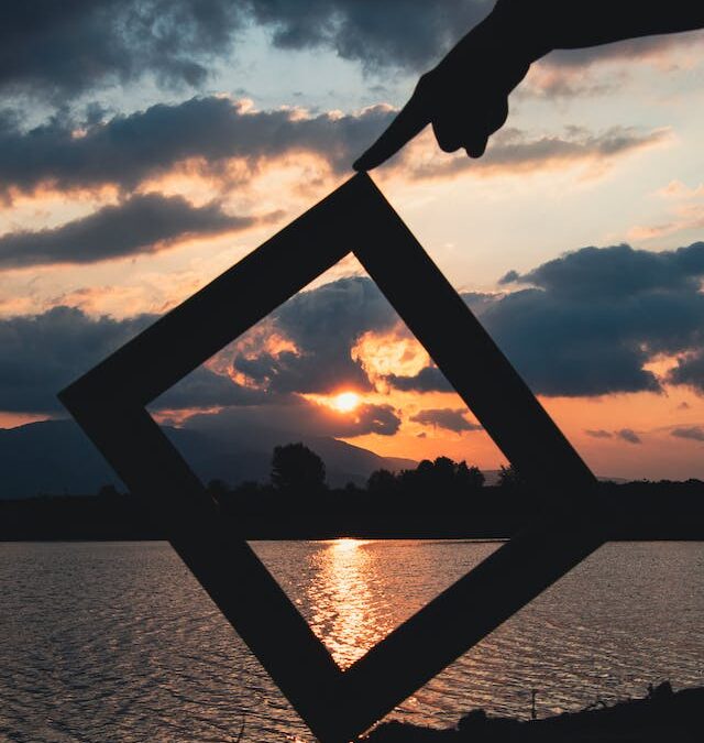Silhouette of a photo frame held against a breathtaking sunset sky, symbolizing the concept of reframing one's perspective to embrace change and new opportunities.